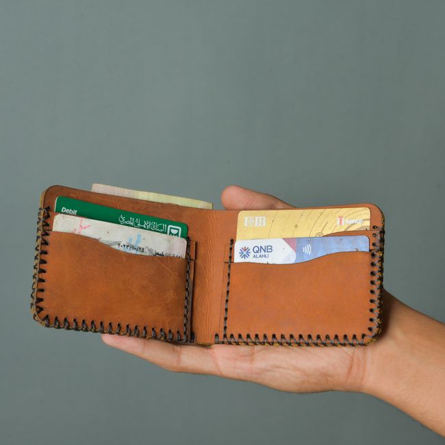 Hand holding a brown bifold wallet